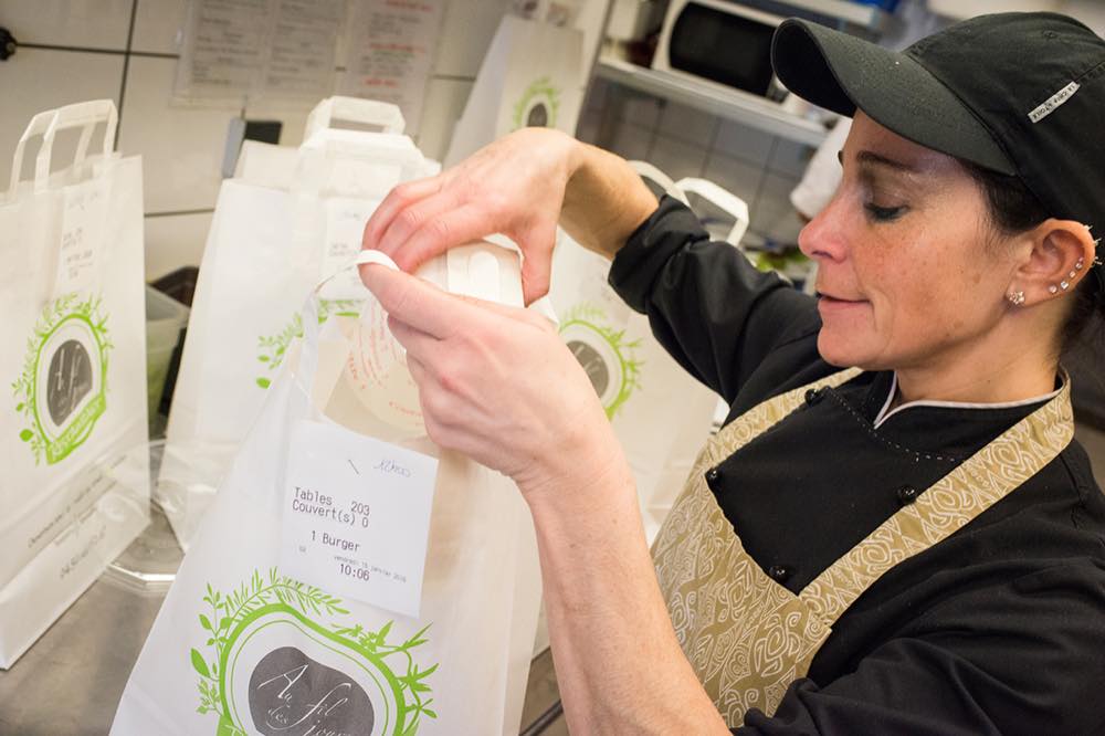 Préparation des commandes à emporter en cuisine : sacs étiquetés au nom du restaurant