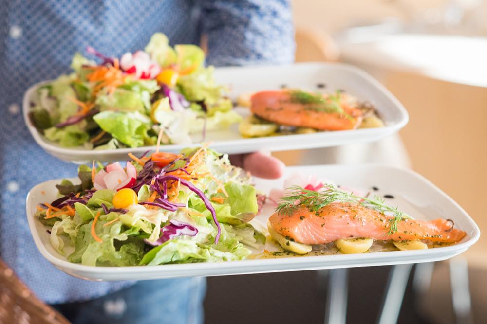 Deux assiettes de saumon et salade portées en salle par un membre de l'équipe